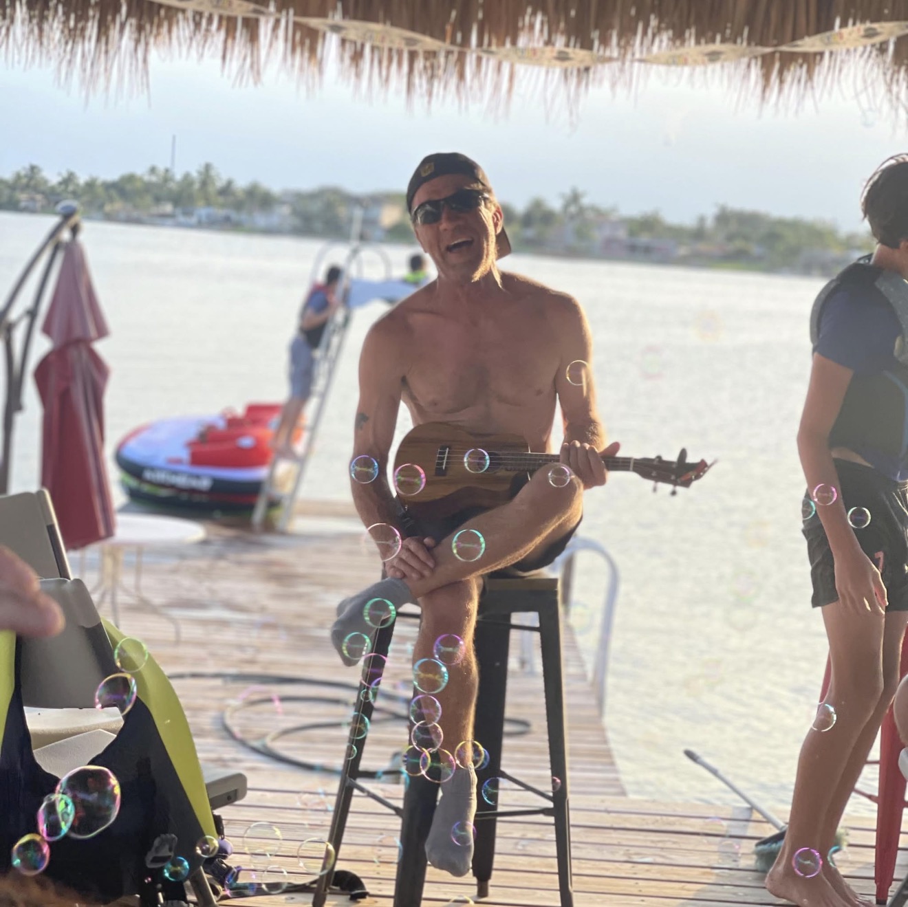 Carl Potts smiling with a small stringed instrument while sitting by the water